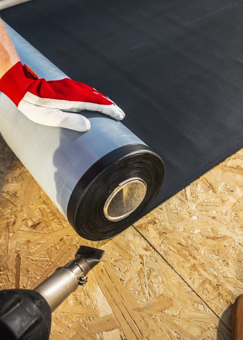Roof Worker with Roll of EPDM Rubber Membrane Material Preparing to Cover Plywood Roof