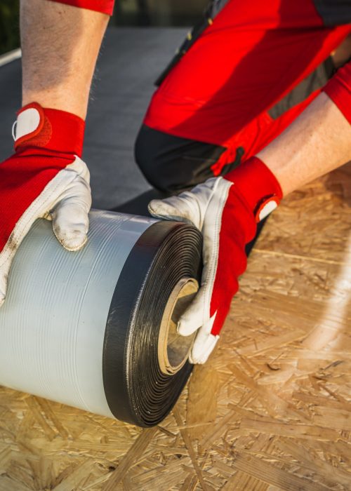 Caucasian Roofing Worker Preparing a Roll of EPDM Roof Membrane Material. Construction Industry Theme.