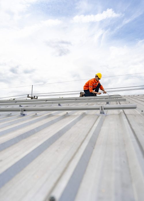 Technician in safety uniform and helmet kneeling on a rooftop, using a drill for precise installation work. A scene highlighting safety, professionalism, and technical expertise in construction.