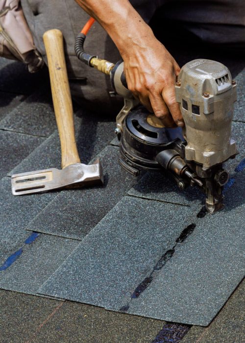 An air nail gun is used by construction worker to install new bitumen shingles on roof