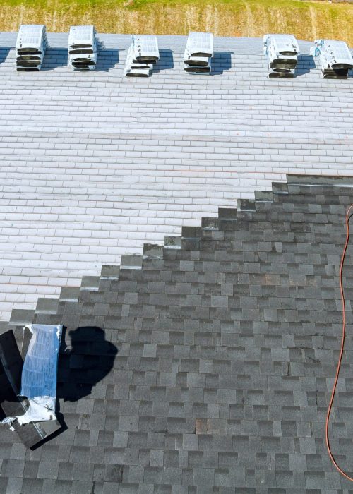 Aerial view in worker hands installing bitumen roof shingles with air hammer and nail