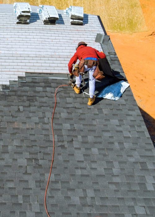 Aerial view in worker hands installing bitumen roof shingles with air hammer and nail