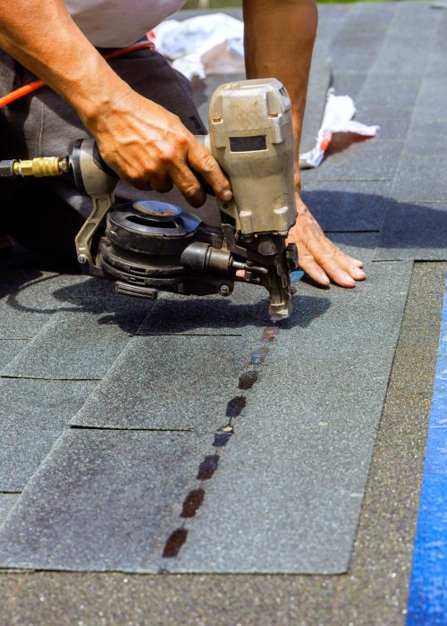 Construction worker used an air pneumatic nail gun when installing new bitumen shingles on roof