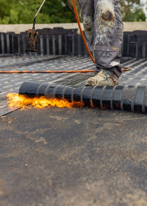 Workers placing a vapor barrier on the roof using a propane gas torch for welding bitumen sheets.