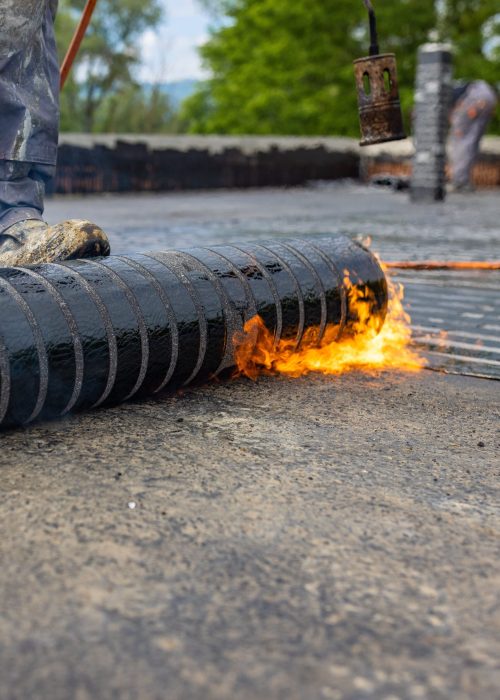 A worker placing a vapor barrier on the roof using a propane gas torch for welding bitumen sheets