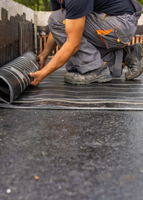 Worker laying the vapor barrier for the roof, bituminous membrane to be welded with flame