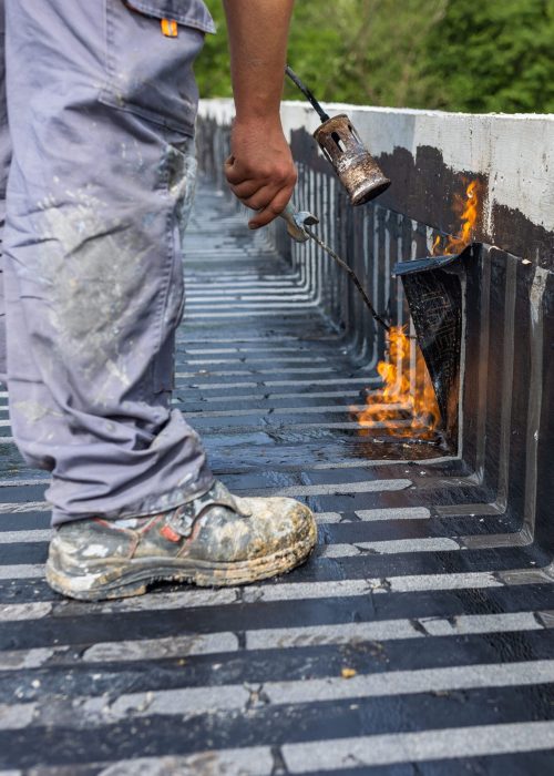 A worker placing a vapor barrier on the roof using a propane gas torch for welding bitumen sheets